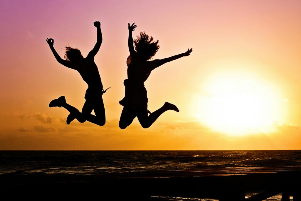 Two people, silhouetted, jumping for joy against a background featuring a sunset