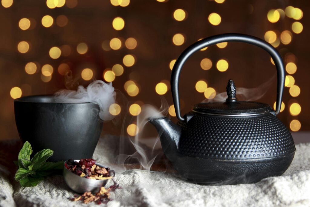 A black pot and black cup on a fluffy tablecloth against a fairy light background.