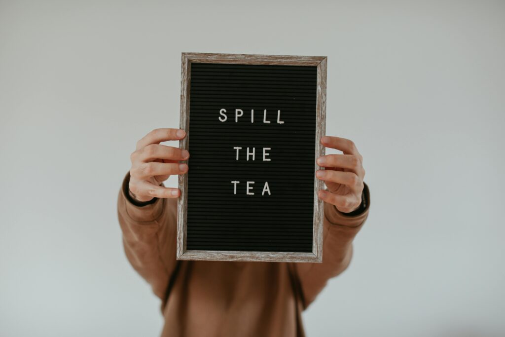 A person holding a sign in front of them which reads "Spill the tea"