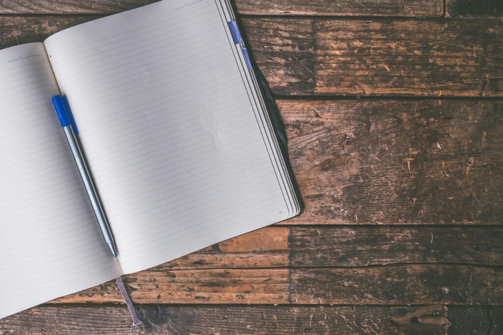 A lined journal on a wooden table with a blue pen