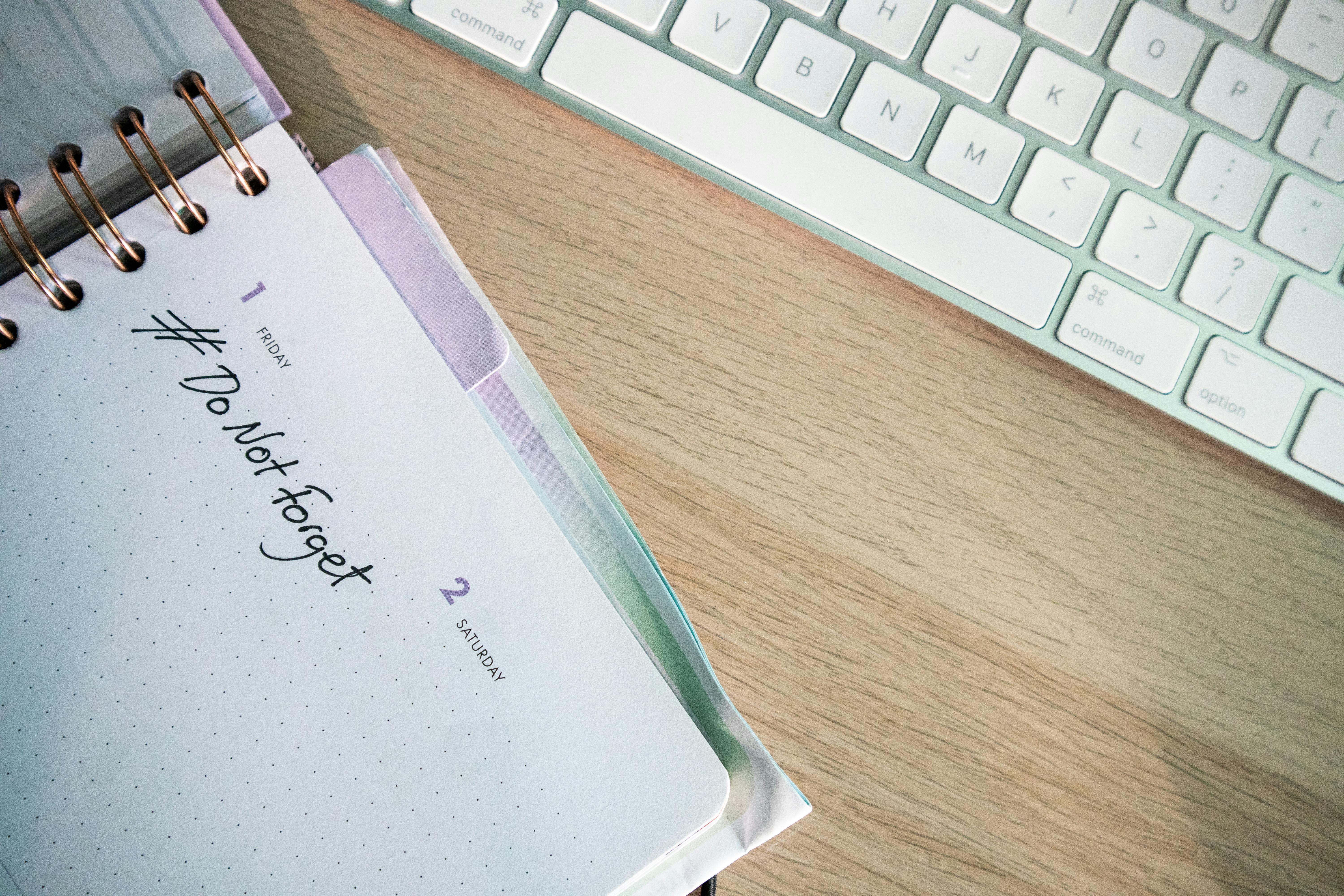 A diary reading #DoNotForget beside a computer keyboard
